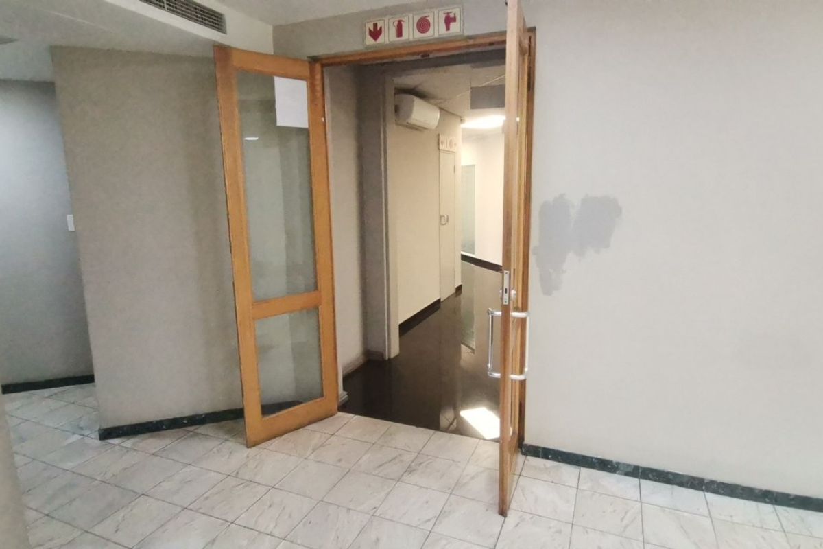 A vacant commercial hallway featuring tiled flooring, wooden door frames with glass panels, and an installed air conditioning unit.