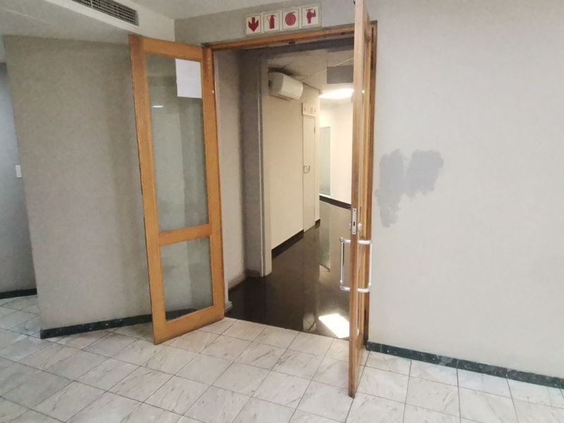 A vacant commercial hallway featuring tiled flooring, wooden door frames with glass panels, and an installed air conditioning unit.