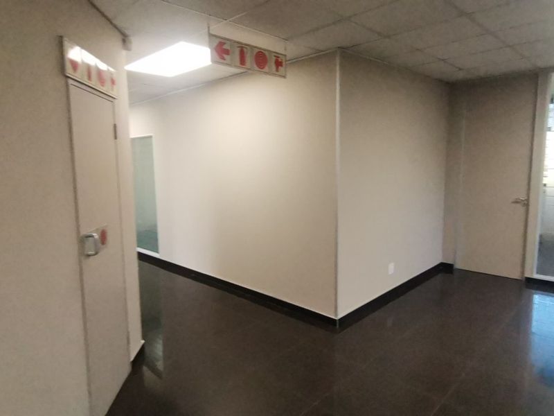 A clean, modern commercial hallway featuring tiled flooring, suspended ceiling with recessed lighting, and glass partition office access.