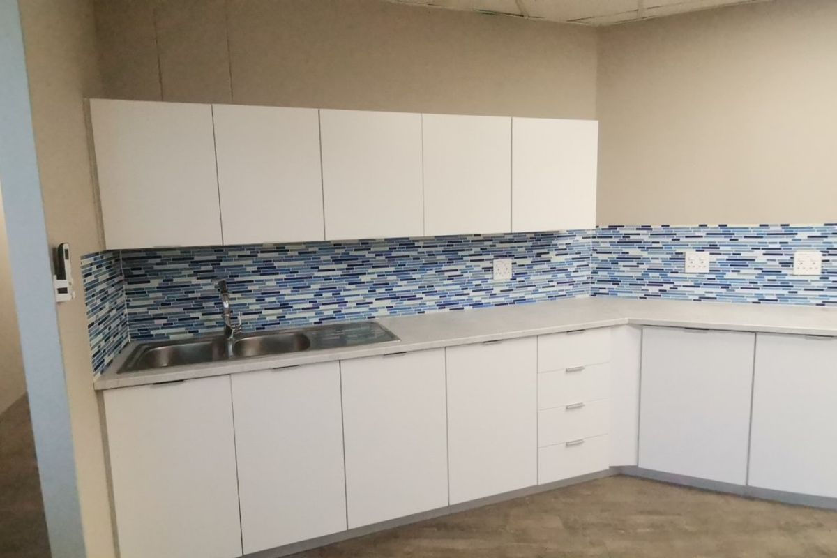 A functional kitchenette featuring white built-in cabinetry, a stainless steel sink, and a decorative blue mosaic tile backsplash.