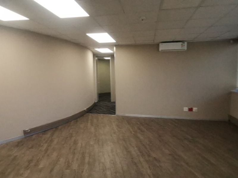 A vacant commercial office space featuring vinyl plank flooring, recessed ceiling lighting, and a wall-mounted split-system air conditioning unit.