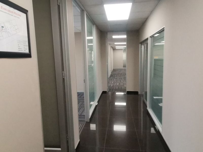 A clean, modern commercial hallway featuring polished tiled flooring, glass partition walls, and recessed ceiling lighting, providing a professional office environment.