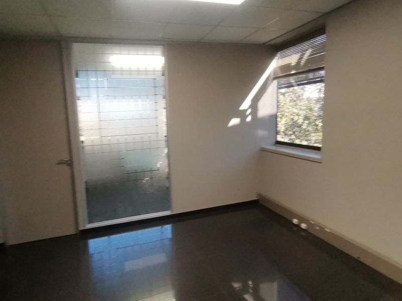 A vacant office space featuring tiled flooring, a frosted glass door, and a window with fitted blinds.