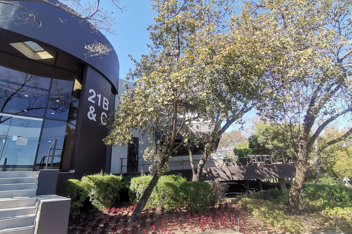 Front exterior view of a modern commercial building featuring a curved facade, glass entrance, and landscaped garden area.