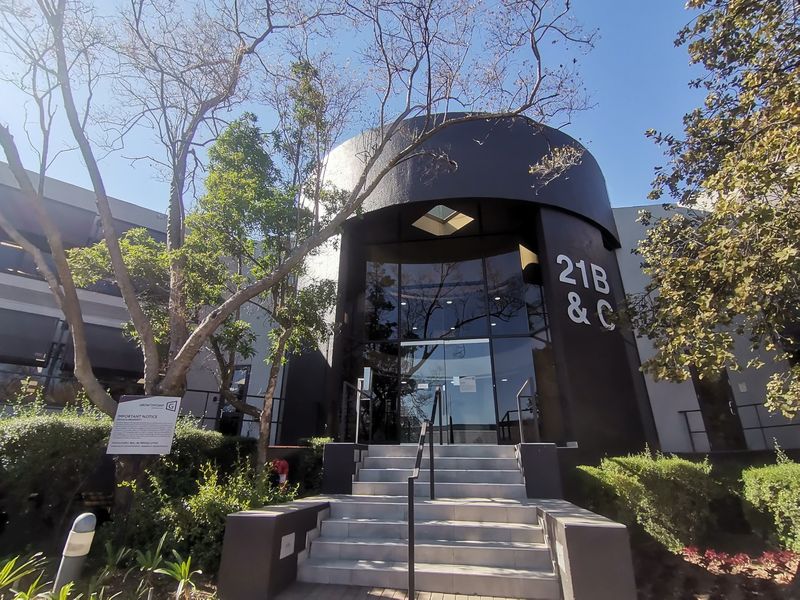 Front entrance of a commercial building featuring a modern glass facade, concrete steps with metal handrails, and prominent signage.