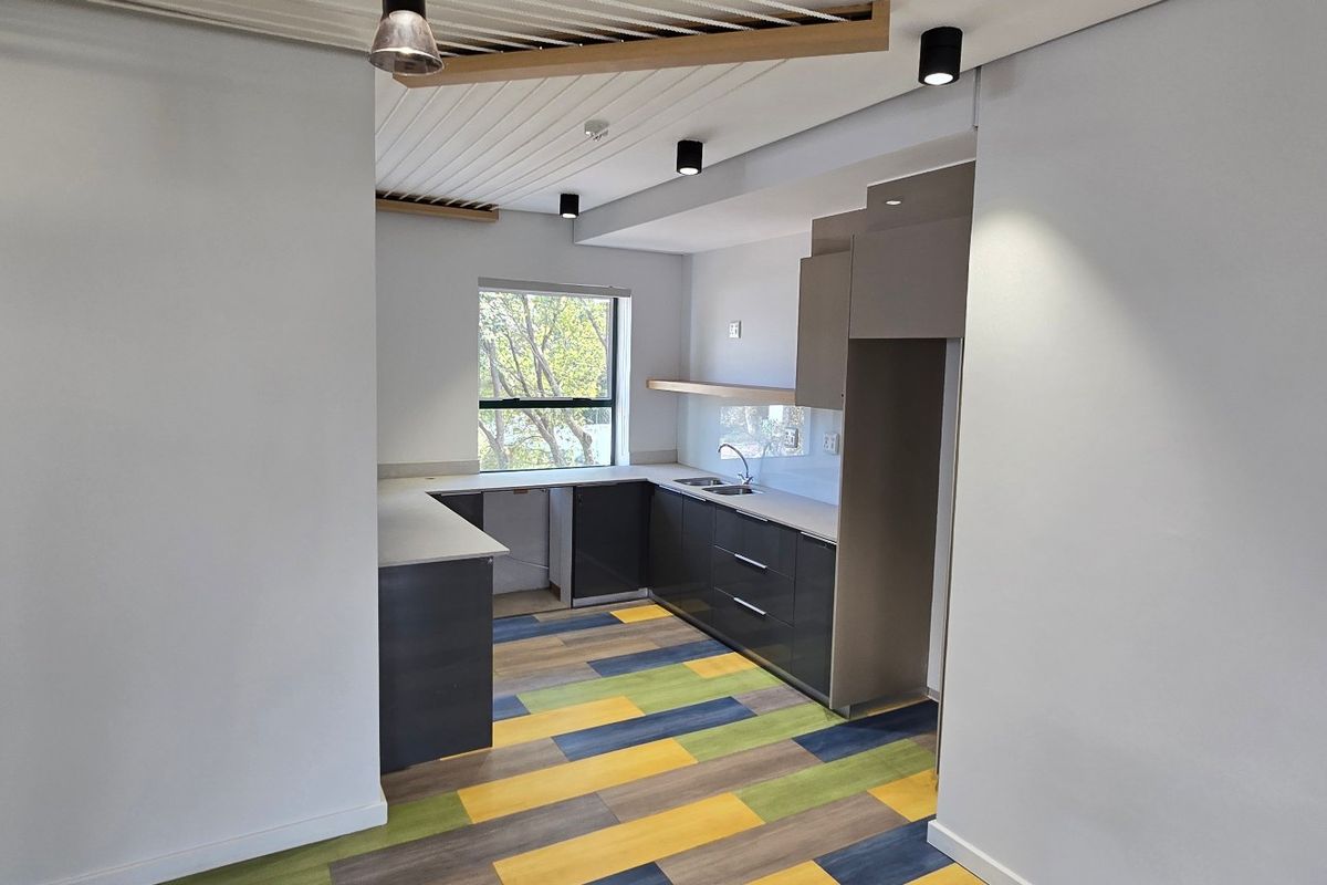 A modern, empty kitchen featuring sleek dark cabinetry, light countertops, a stainless steel sink, and vibrant multi-colored laminate flooring.