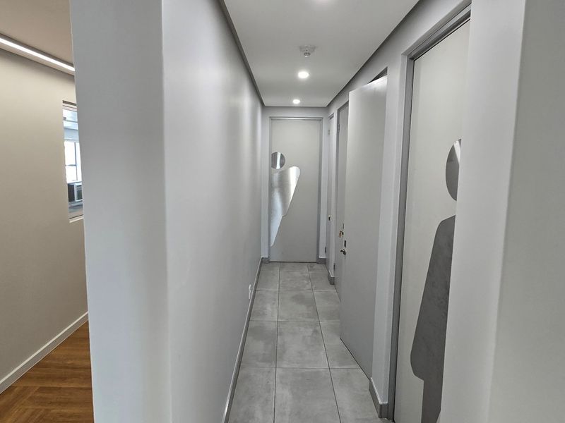 A clean, modern commercial hallway featuring neutral grey tones, tiled flooring, and recessed ceiling lighting leading to multiple office or facility doors.