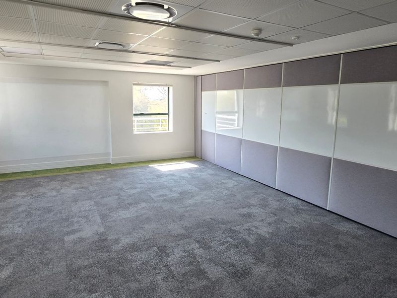 A clean, empty commercial office space featuring carpeted flooring, recessed ceiling lights, and integrated whiteboard wall panels, suitable for a professional workspace.