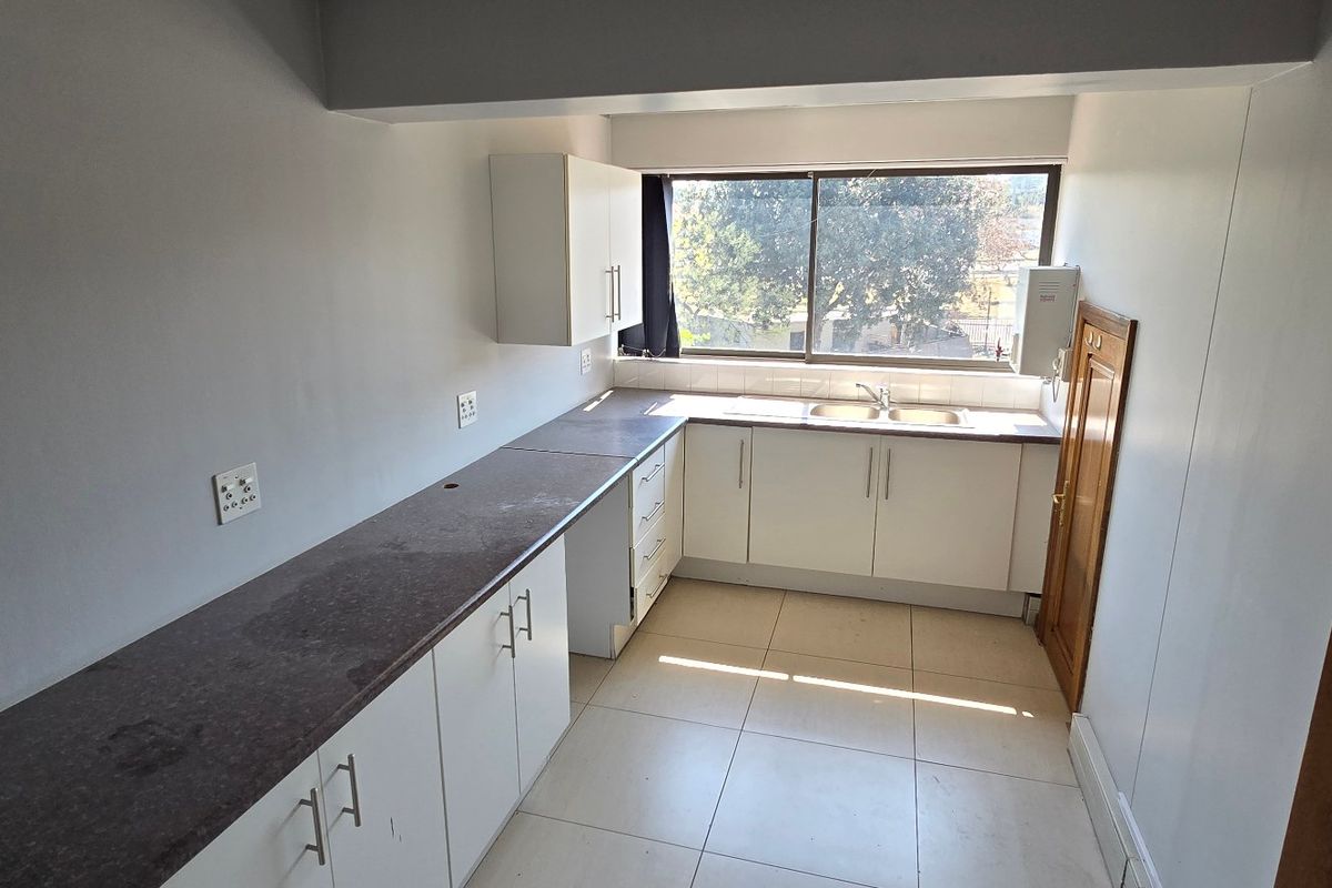 A functional, empty kitchen featuring white cabinetry, dark laminate countertops, tiled flooring, and a double bowl sink with natural light from a sliding window.