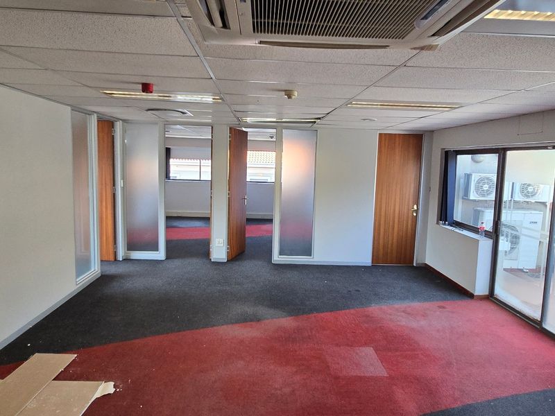 An empty commercial office space featuring suspended ceilings, ducted air conditioning, and glass partition doors, offering a versatile layout for professional use.