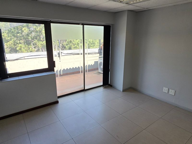 A bright, empty office space featuring tiled flooring, a suspended ceiling, and a sliding glass door providing access to an outdoor area.