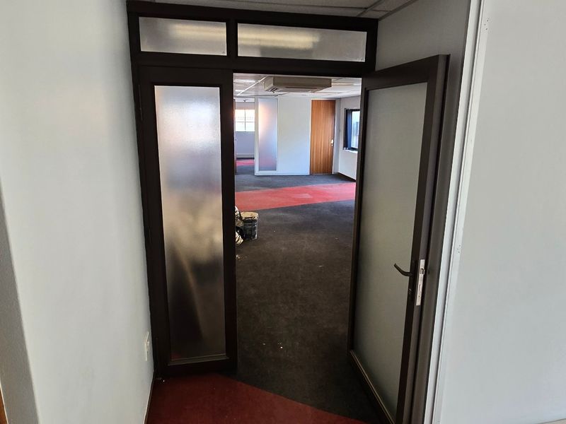 An empty office space featuring a frosted glass door, suspended ceiling, and carpeted flooring, ready for commercial fit-out.