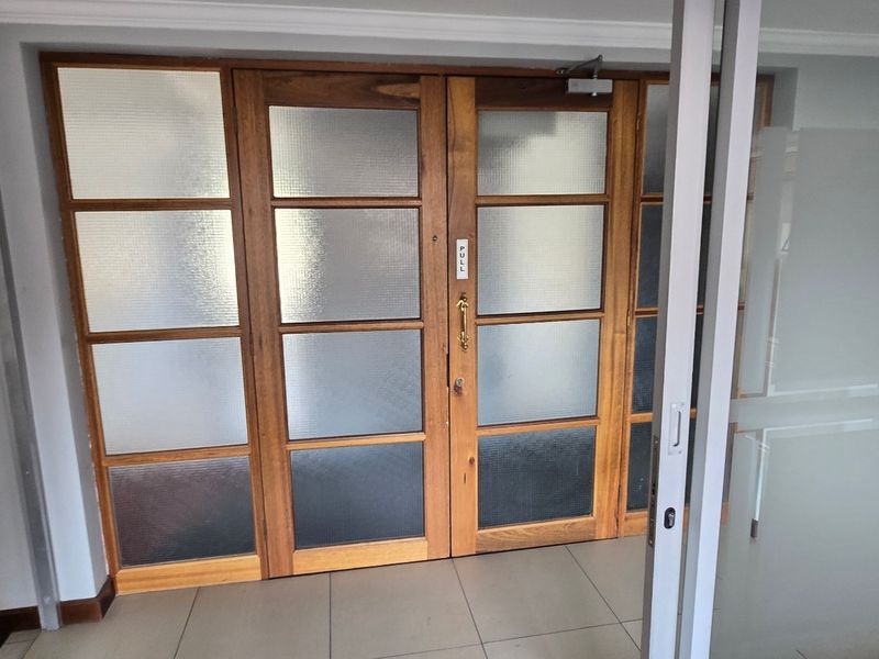 A clean commercial entrance area featuring timber-framed double doors with frosted glass panels and neutral ceramic floor tiling.