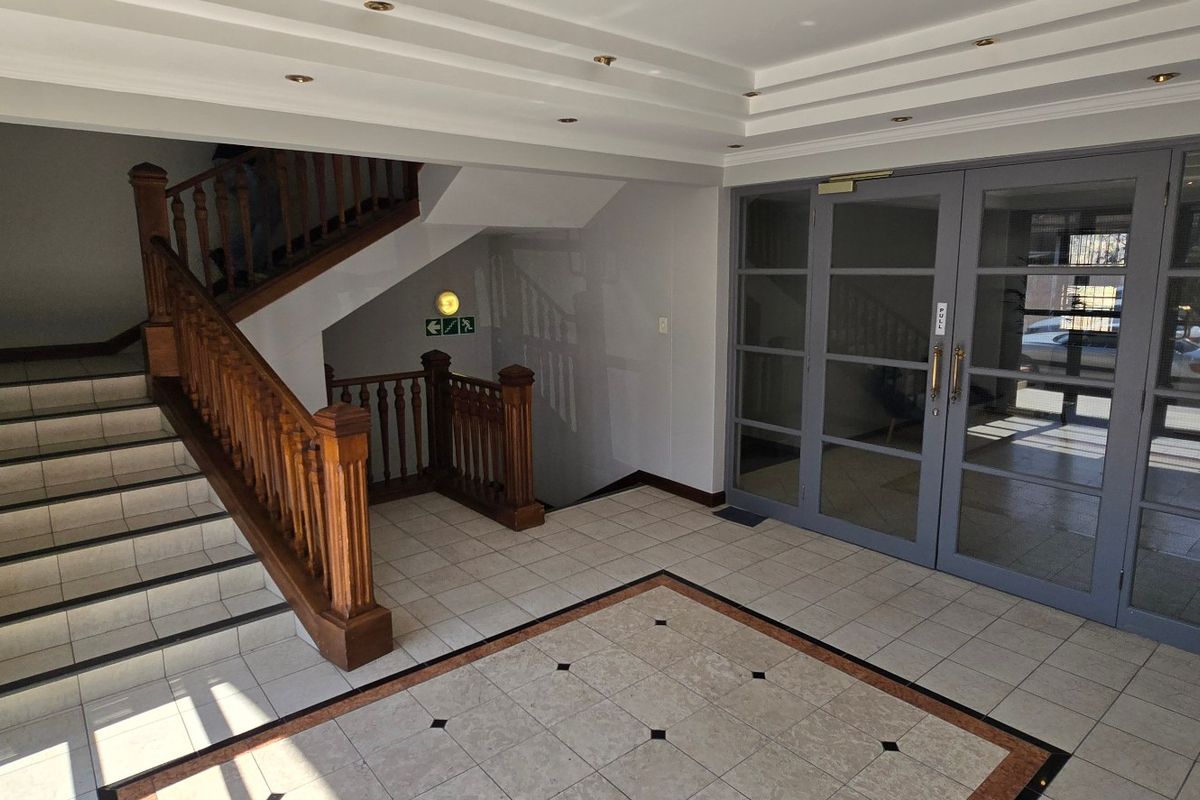 A spacious commercial building entrance lobby featuring tiled flooring, a wooden staircase with balustrade, and large glass-panelled doors.