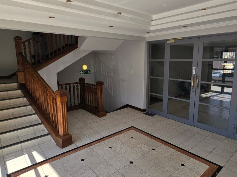 A spacious commercial building entrance lobby featuring tiled flooring, a wooden staircase with balustrade, and large glass-panelled doors.