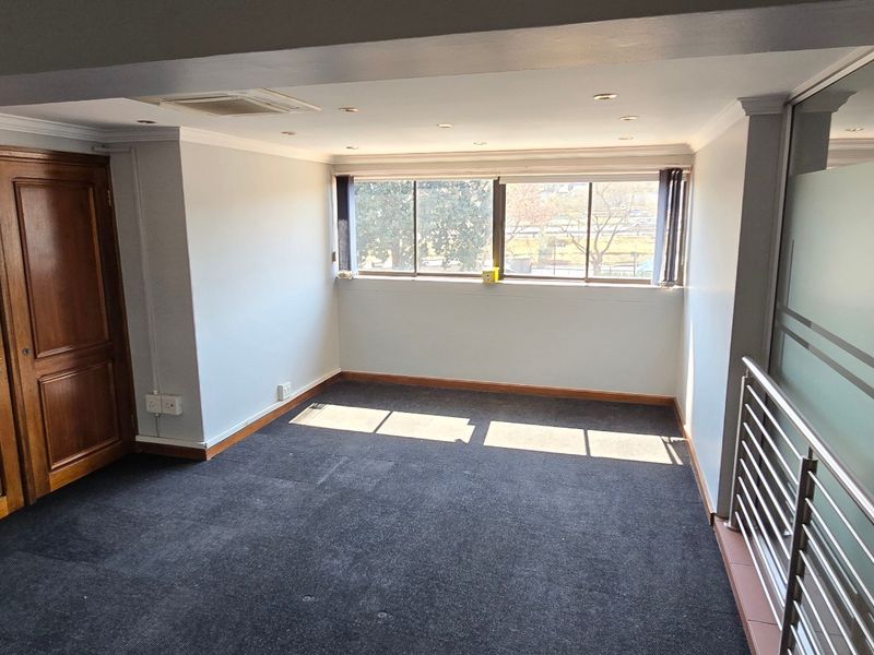 A bright, empty office space featuring carpeted flooring, recessed downlighting, timber double doors, and a modern frosted glass partition with a metal balustrade.