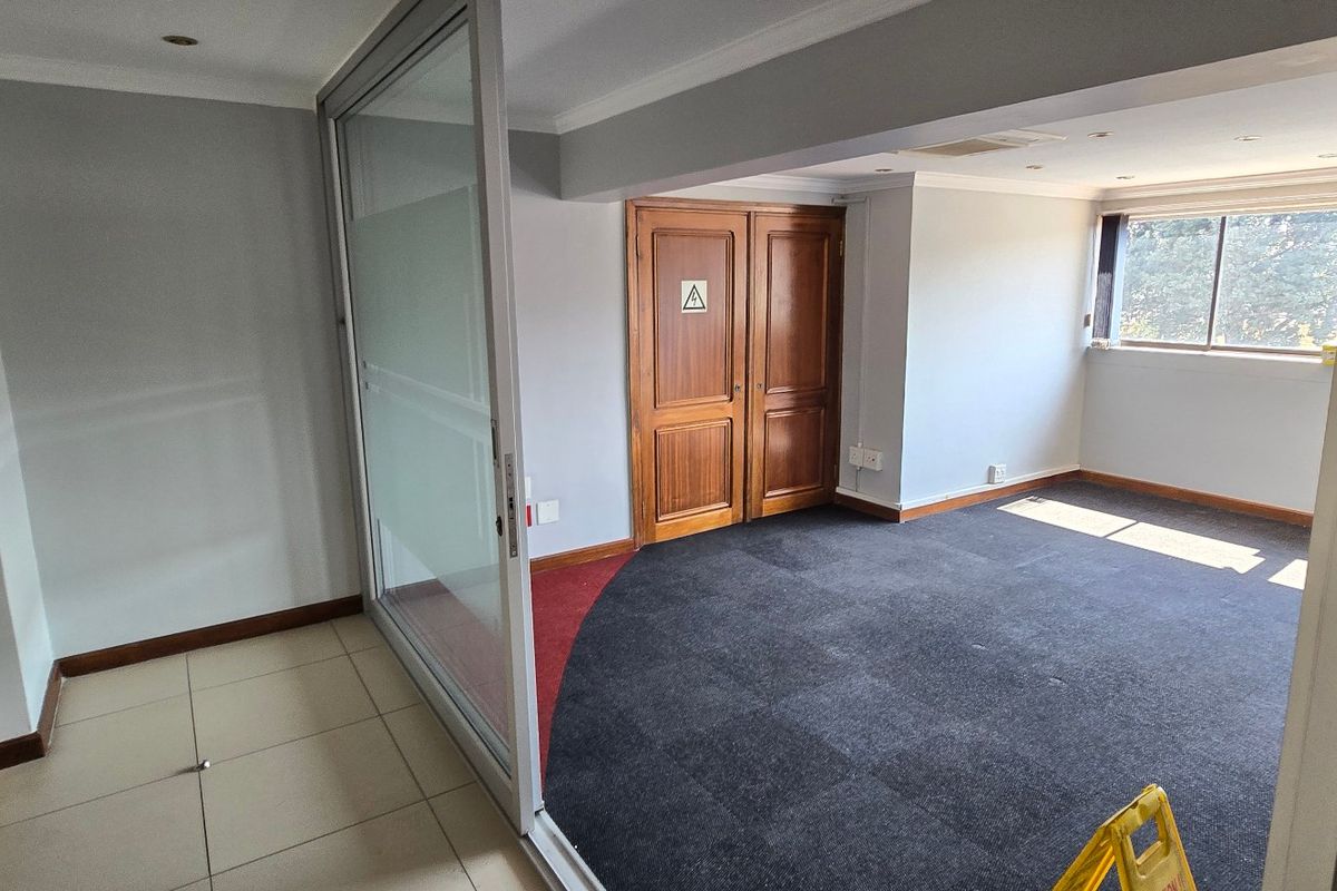 An empty commercial office space featuring a sliding glass partition, timber double doors, and a combination of carpet and tiled flooring.