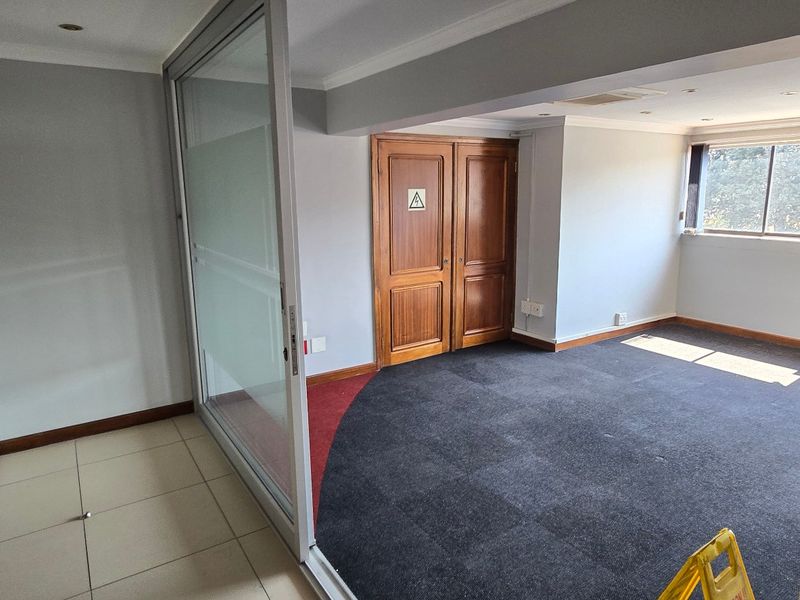 An empty commercial office space featuring a sliding glass partition, timber double doors, and a combination of carpet and tiled flooring.