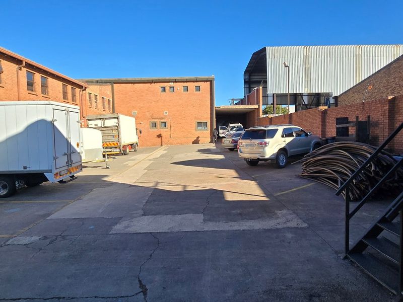 Rear industrial yard area featuring exposed brick building facades, concrete paving, and a perimeter wall with access to a metal staircase.