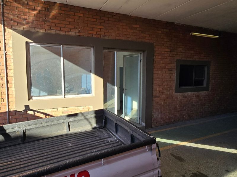 Industrial garage space featuring exposed brick walls, concrete flooring, and a secure roller shutter door with integrated office or utility access.