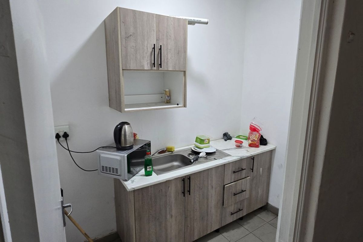 A compact kitchenette featuring modern wood-look laminate cabinetry, a stainless steel sink, and tiled flooring, suitable for a small office or industrial utility space.