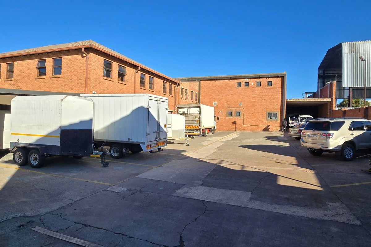 Spacious industrial rear yard featuring brick building facades, concrete paving, and covered parking facilities suitable for logistics or storage operations.