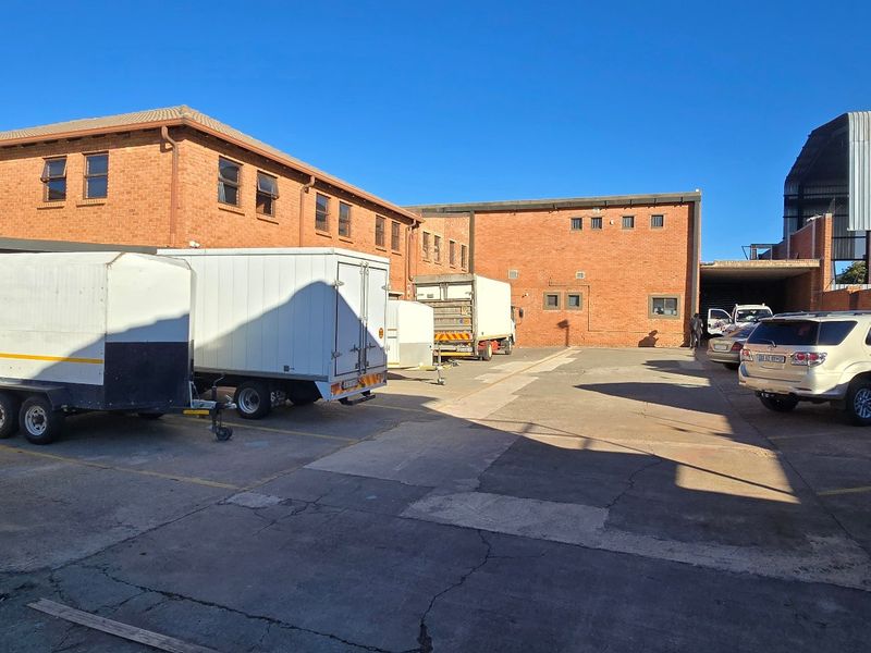 Spacious industrial rear yard featuring brick building facades, concrete paving, and covered parking facilities suitable for logistics or storage operations.