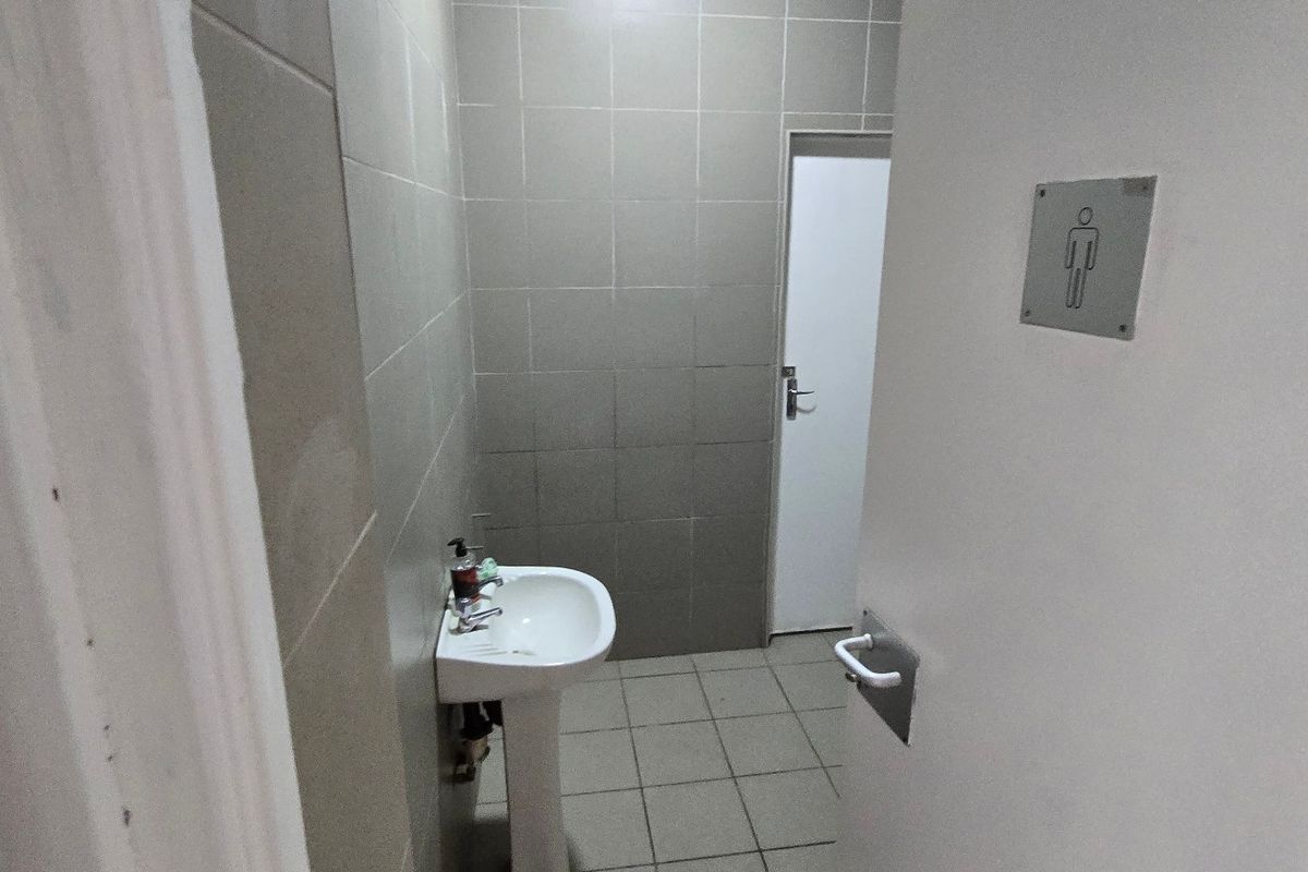 A functional industrial restroom facility featuring a pedestal washbasin, tiled walls, and tiled flooring.