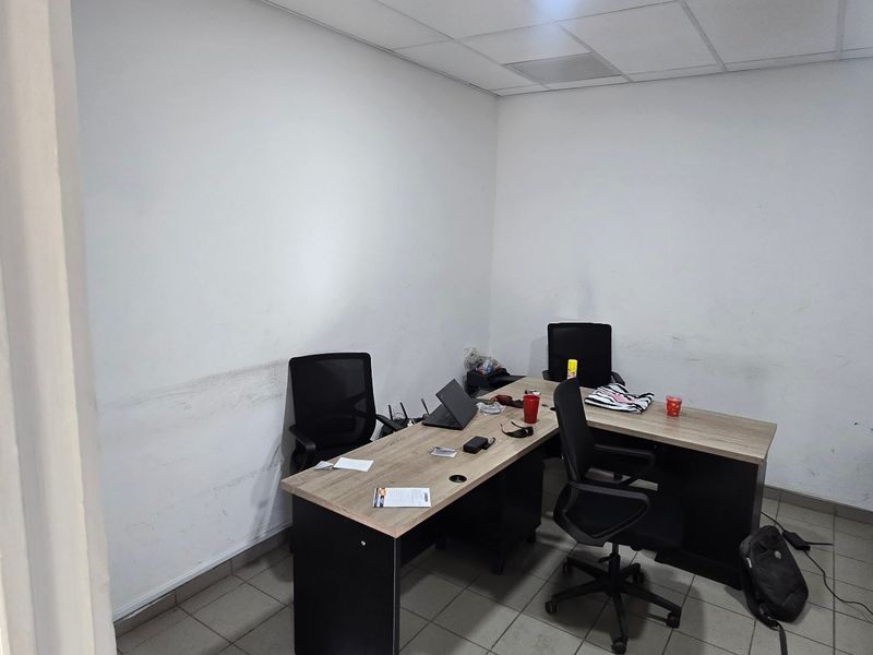 A functional office space featuring tiled flooring and a suspended ceiling, currently requiring cosmetic wall maintenance.