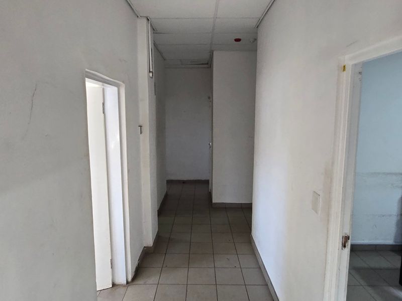 A functional industrial hallway featuring tiled flooring and a suspended ceiling, providing access to multiple office or utility rooms.
