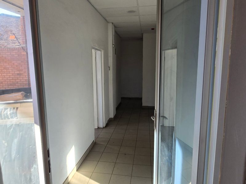 A vacant industrial hallway featuring tiled flooring, a suspended ceiling, and an aluminium-framed glass entrance door.