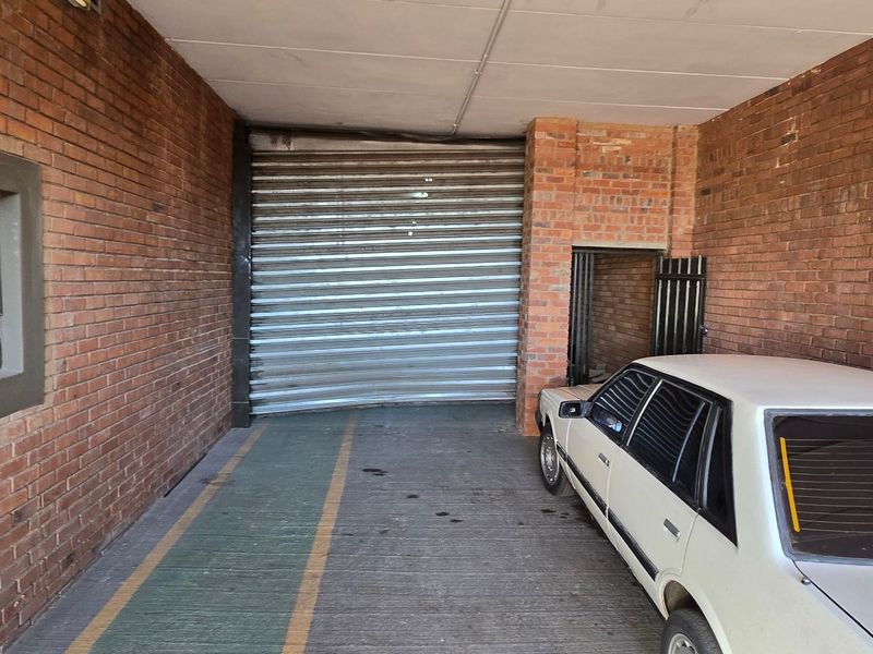Industrial garage space featuring exposed brick walls, concrete flooring, and a large roller shutter door for vehicle access.