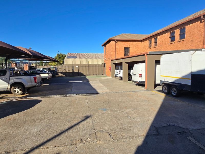 Industrial property exterior featuring a paved parking area with shade cloth carports and secure perimeter fencing.