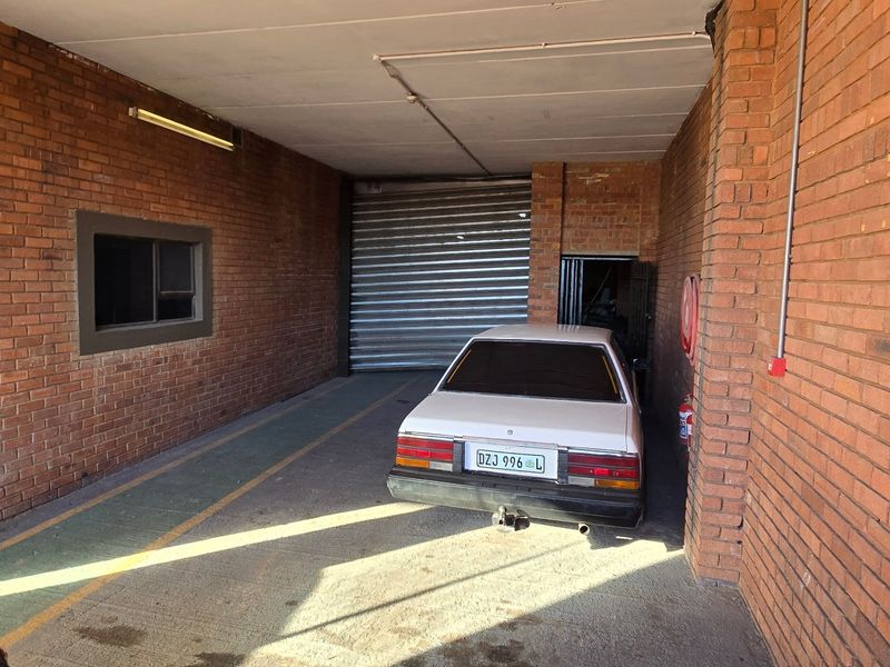 Industrial garage space featuring exposed brick walls, concrete flooring, and a secure roller shutter door, providing functional vehicle storage or utility access.