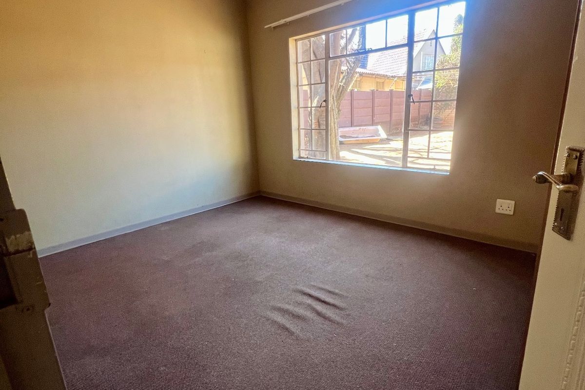 An empty bedroom featuring dark carpeting, a steel-framed window, and neutral wall finishes, offering a blank canvas for potential renovation or staging.