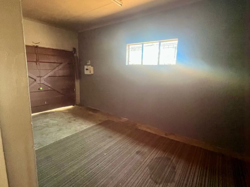A vacant garage space featuring concrete flooring, a single window with security bars, and an integrated electrical distribution board.