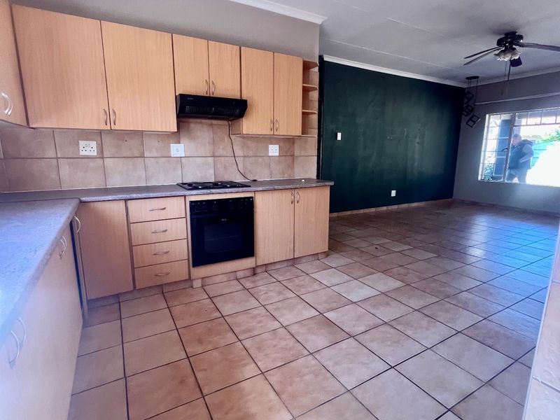 Open-plan kitchen and living area featuring tiled flooring, built-in cabinetry, and integrated cooking appliances in a functional, vacant space.