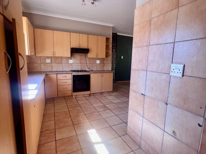 A functional kitchen featuring light wood cabinetry, built-in oven and hob, tiled flooring, and a tiled feature wall.
