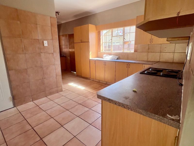 A functional kitchen featuring built-in wooden cabinetry, laminate countertops, an integrated electric hob, and tiled flooring throughout.