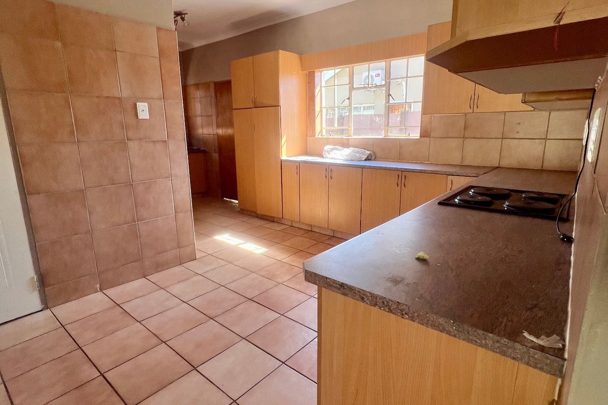 A functional kitchen featuring built-in wooden cabinetry, laminate countertops, an integrated electric hob, and tiled flooring throughout.