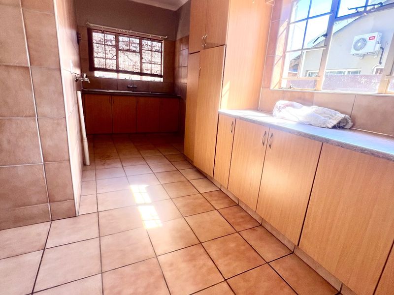 A spacious, empty kitchen featuring built-in wooden cabinetry, tiled flooring, and ample natural light from multiple windows.