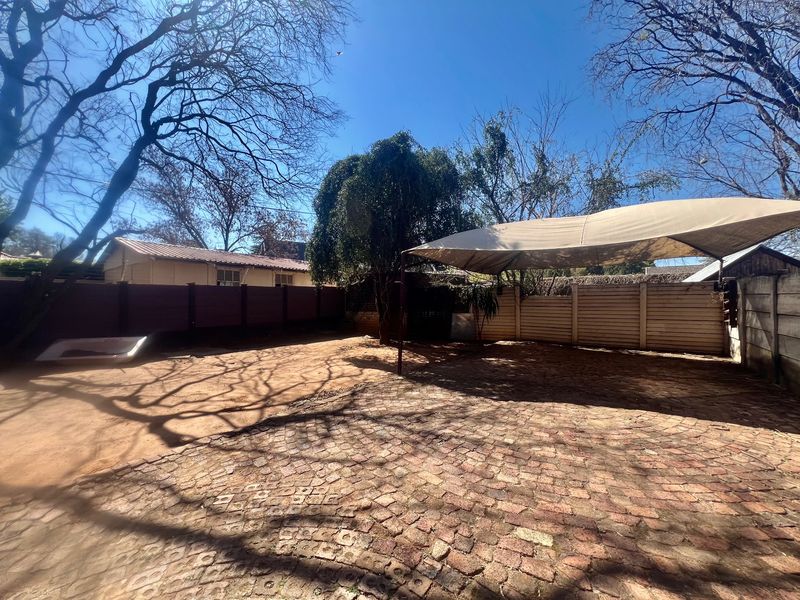 A spacious rear outdoor area featuring a paved surface, shade sail structure, and perimeter fencing, offering potential for landscaping or outdoor living development.