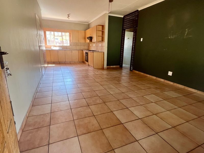 An open-plan living and kitchen area featuring tiled flooring, built-in cabinetry, and a ceiling fan, offering a blank canvas for potential updates.