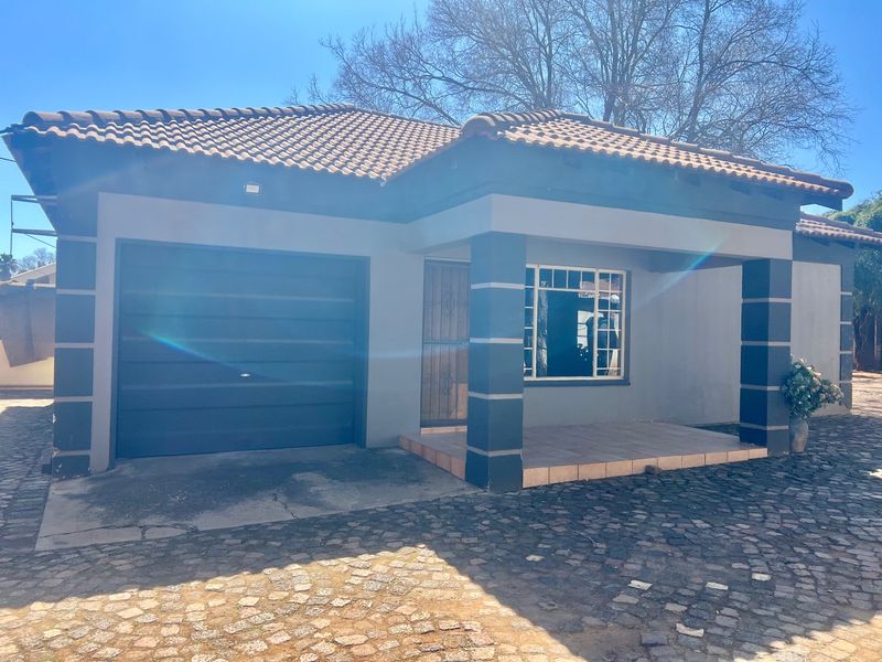 Front elevation of a single-story apartment featuring a tiled roof, integrated garage, and a covered entrance porch with cobblestone driveway access.