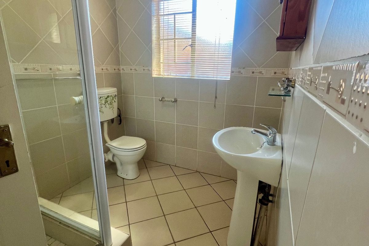 A functional bathroom featuring a pedestal basin, toilet, and a glass-enclosed shower with neutral wall and floor tiling.