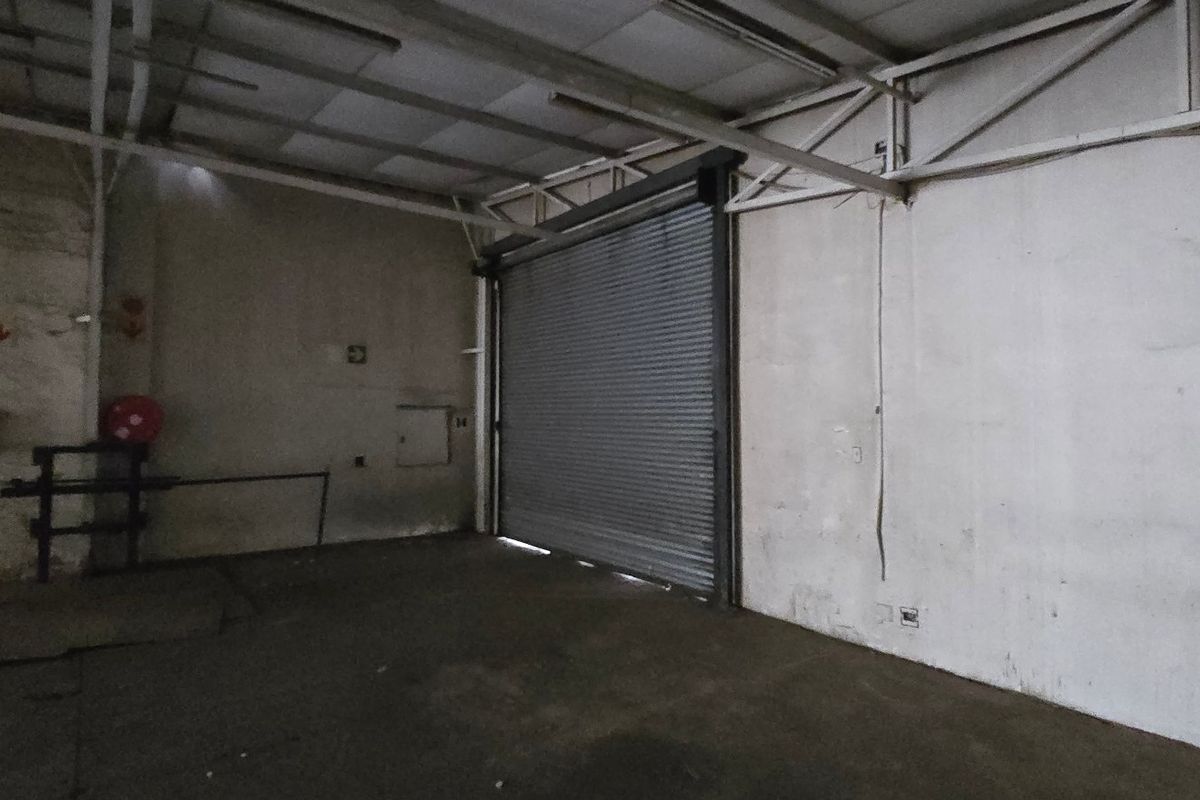 An empty industrial utility space featuring exposed steel roof trusses, concrete flooring, and a large roller shutter door for vehicle or equipment access.