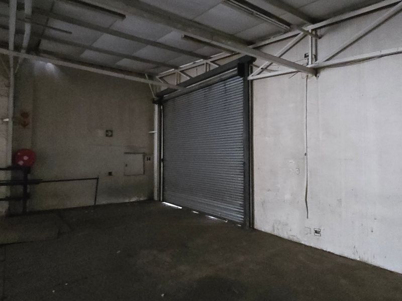 An empty industrial utility space featuring exposed steel roof trusses, concrete flooring, and a large roller shutter door for vehicle or equipment access.
