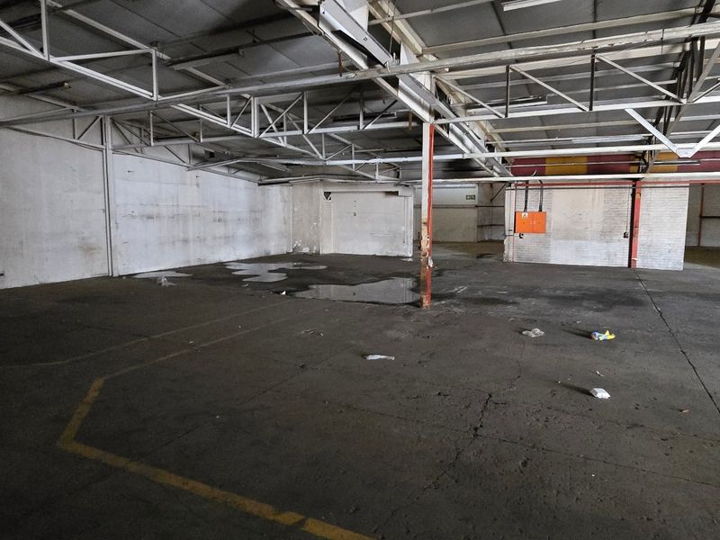 Spacious industrial warehouse unit featuring exposed steel roof trusses, concrete flooring, and a large roller shutter door for easy access.