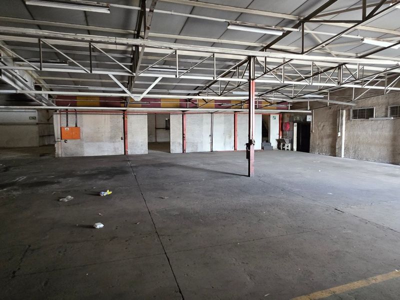Expansive industrial warehouse space featuring high ceilings with exposed steel trusses, concrete flooring, and functional support columns.