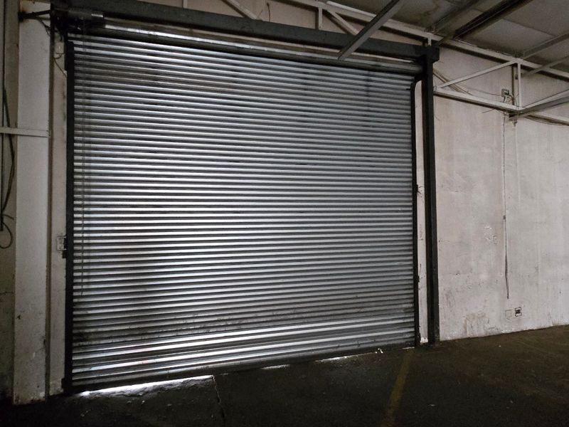 Spacious industrial garage area featuring a large roller shutter door, exposed steel roof trusses, and durable concrete flooring.